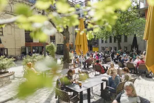 Außenaufnahme des Hofes mit Menschen an Tischen in der Sonne und großen Sonnenschirmen