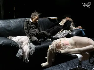 verschiedene Puppen auf einer schwarzen Couch im Bühnenbild
