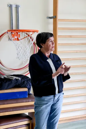 Birgit Deininger im Gespräch, hinter ihr ist eine Sprossenwand und ein Basketballkorb zu erkennen. 