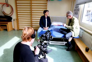 Behind the scenes: Birgit Deininger und Oliver Reese unterhalten sich auf der Behandlungsliege sitzend, davor kniet der Kameramann.