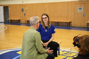 Oliver Reese und Wiebke Schwartau sitzen in der Mitte der Sporthalle, es ist Reeses Rücken zu sehen und Schwartau frontal. 