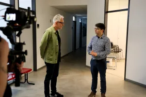 Oliver Reese und Taylan Akdag begrüßen sich auf den Fluren der TU, am Bildrand ist eine Kamera zu erkennen. 