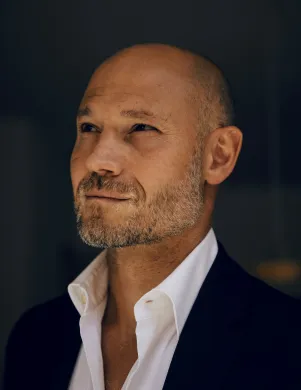 Mann (Omri Boehm) im Halbprofil vor schwarzem verschwommenem Hintergrund in Hemd und Jackett