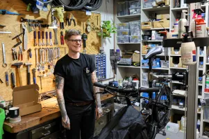 Jenny Andersen steht in der Werkstattmitte und lacht, vor ihr ist ein schwarzes Fahrrad zu erkennen.