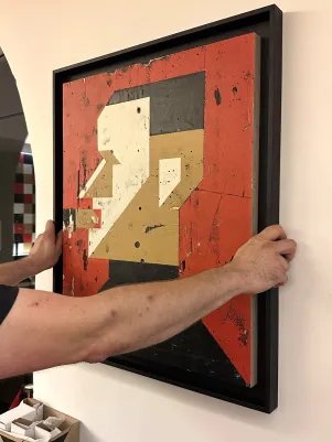 Ein stilisiertes Portrait von Bertolt Brecht wird angebracht, es sind Arme zu erkennen, die den Rahmen festhalten. 