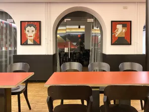 Ansicht der beiden Portraits in der Kantine, vorn sind Tische und Stühle zu erkennen, zwischen den beiden Bildern befindet sich die Tür zum Kantinennebenraum.