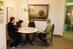 Behind the scenes im Büro: an einem runden Tisch sitzen von links nach rechts der Kameramann, Jacqueline Dey und Oliver Reese. 