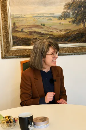 Portrait von Jacqueline Dey im Gespräch, sie lehnt sich etwas vor und lacht. 