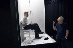 Jens Harzer sitzt im erhöhten Bühnenbild, vor im steht Oliver Reese und gestikuliert. 