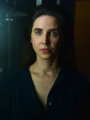 Schauspielerin Marina Galic in Frontalansicht, schaut direkt in die Kamera. Sie trägt eine schwarze Bluse, steht vor schwarzer Wand.