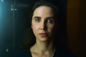 Schauspielerin Marina Galic in Frontalansicht, schaut direkt in die Kamera. Sie trägt eine schwarze Bluse, steht vor schwarzer Wand.