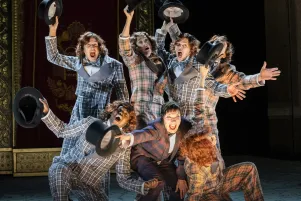 24)	Sieben Personen in karierten Anzügen stehen eng zusammen und strecken schwarze Zylinderhüte in die Luft.