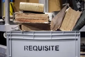 Eine graue Plastikkiste auf der "Requisite" steht. Darin sind verschiedene alte, dicke Bücher. 
