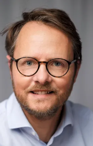 close up von Michael Meyer-Resende, in Hemd. Er trägt eine Brille und schaut in die Kamera.