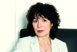 Sabine Adler in weißem Blazer vor weißer Wand. 