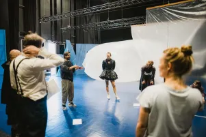 Im Kreis auf der Bühne stehen der Regisseur und das Ensemble. Er erklärt etwas, des Rest hört zu und bewegt sich frei. 