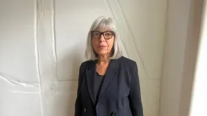 Rebecca Harms in dunklem Blazer vor heller Wand. Sie trägt Brille und schaut in die Kamera.