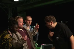 Im linken Bildteil sind Joyce Sanhá, Peter Moltzen und Jannik Mühlenweg zu erkennen, die sich dem vorbeugenden und gestikulierenden Regisseur im rechten Bildteil zuwenden. 