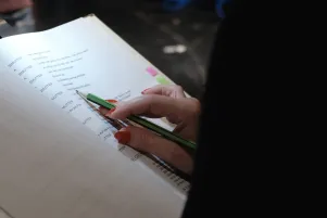 Schnappschuss vom Textbuch, jemandes Hand ist zu erkennen, ein Bleistift zeigt auf die Stelle im Text, die gerade gesprochen wird. 