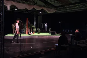 Schnappschuss mit Blick auf die Bühne. Jannik Mühlenweg tritt von links auf, im Dunklen ist der Regisseur auf einem Stuhl sitzend zu erkennen. 