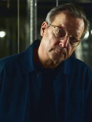 Nahes Portrait von Matthias Brandt, er schaut mit schräg gelegtem Kopf direkt in die Kamera. 