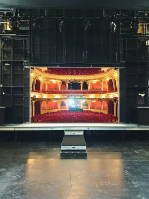 Die große Bühne ist bis auf einen Bühnensteg leer. Der Blick reicht in den hell erleuchteten, leeren Zuschauerraum. 