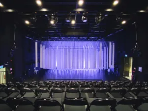 Blick auf die leere Bühne von "Gittersee", die Papierstreifen hängen ruhig herab, das Licht leuchtet violett. 