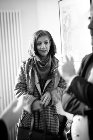 Schnappschuss in Schwarzweiß von Mina Khan. Sie ist in der Bewegung eingefroren und scheint jemandem aufmerksam zuzuhören. 