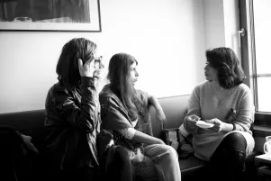 Schnappschuss von drei Frauen, die auf einer Bank sitzen, einander zugewandt sind und miteinander sprechen. 