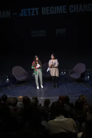 Blick auf die Bühne des Neuen Hauses. Die Stühle auf dem Podium sind noch leer, Daniela Sapehri begrüßt das Publikum. 