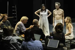 Auf der Bühne stehen Constanze Becker und Jens Harzer in Probenkostümen, im vorderen Bildteil ist das Produktionsteam zu erkennen, Regisseur Johan Simons spricht mit Becker und Harzer.