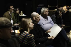 Das Produktionsteam schaut dicht aneinandergerückt auf den Probenprozess. Regisseur Johan Simons ist im rechten Bildteil zu erkennen.