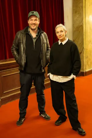 Max Czollek und Marion Brasch stehen vor den Garderobentresen im Großen Haus, sie sind vollständig zu erkennen und stehen nah beieinander.