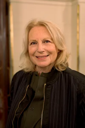 Portrait von Maren Kroymann im Foyer des Großen Hauses. Sie hält sich leicht seitlich und lächelt direkt in die Kamera.