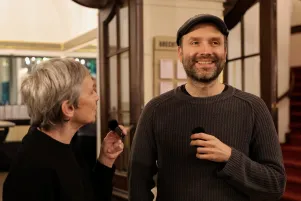 Schnappschuss von Marc-Uwe Kling während der Begrüßung im Foyer des Großen Hauses. Er hält ein kleines Mikrofon in der Hand und lacht. Marion Brasch schaut ihn an. 