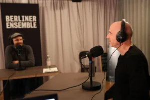 Schnappschuss von der Podcastaufnahme. Marc-Uwe Kling und Paul Herwig unterhalten sich, beide sitzen vor großen Mikrofonen und tragen Kopfhörer. 