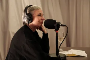 Schnappschuss von Marion Brasch während der Podcastaufnahme. Sie ist im Profil zu erkennen, trägt Kopfhörer, stützt das Kinn auf die linke Hand und vor ihr steht ein Mikrofon. 