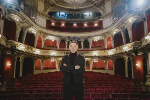 Max Hopp auf der Bühne im Großen Haus des Berliner Ensemble. Im Hintergrund der prunkvoll verzierte Zuschauersaal.