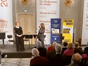 Schnappschuss von der Ansprache der Vorständin des BE-Freundeskreises Regine Lorenz spricht auf einer Bühne stehend in ein Mikrofon. 