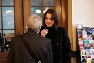 Schnappschuss von Marion Brasch und Christiane Paul während der Begrüßung im Foyer des Großen Hauses. Marion Brasch steht mit dem Rücken zur Kamera und schaut zu Christiane Paul, die wiederum mit einem kleinen Mikrofon in der Hand mit Marion Brasch spricht. 