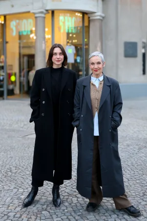 Gemeinsames Portrait von Marion Brasch und Christiane Paul vor dem Berliner Ensemble. Beide tragen lange Mäntel, haben die Hände in die Taschen gesteckt und schauen direkt in die Kamera. 