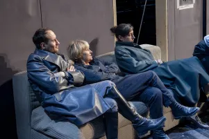 Schnappschuss dreier Spieler:innen in Probenkostümen auf einem Sofa sitzend. 