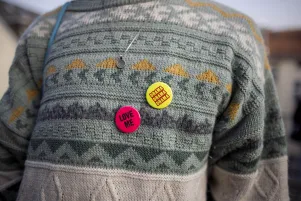 Einige bunte Buttons, auf denen "Love me" und "Drama Drama Drama" steht, sind auf einem gemusterten Pullover befestigt. 