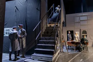 Schnappschuss von der Seitenbühne: Es sind links zwei Spieler im Kostüm zu erkennen, die durch die Position einer Treppe den Blick auf sie abschirmen. Im Hintergrund sind weitere Spieler zu erkennen. 