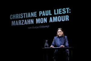 Schnappschuss von der Lesung, Christiane Paul sitzt an einem kleinen Tisch, hinter ihr wird "Christiane Paul liest: Marzahn Mon Amour" an die Wand gebeamt.