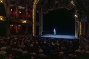 Blick auf die Bühne des Großen Hauses. Der Zuschauerraum ist gefüllt, auf der Bühne steht Oliver Reese. 