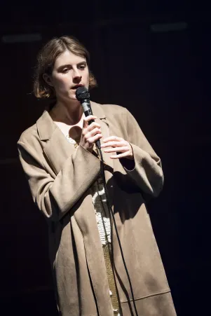 Schnappschuss von Amelie Willberg an einem Mikrofon im Trenchcoat. 
