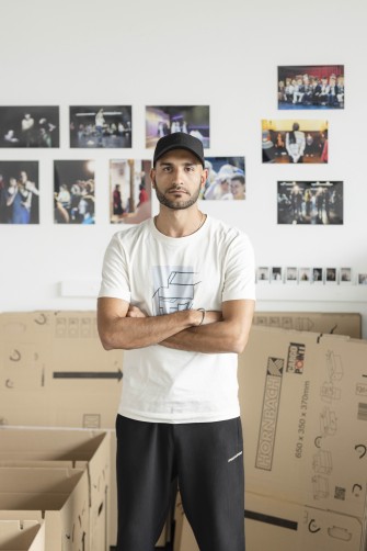 Alireza Daryanavard im Gartenhaus des Berliner Ensembles, hinter ihm Bilder an einer Wand und ein Umzugskarton