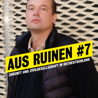 Portrait von Hendrik Bolz im Halbprofil vor dem neuen Haus. Darauf steht "Aus Ruinen #7. Zukunft und Zivilgesellschaft in Ostdeutschland."
