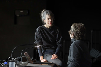 Person in schwarzer Kleidung sitzt auf einem Tisch und unterhält sich mit einer anderen Person